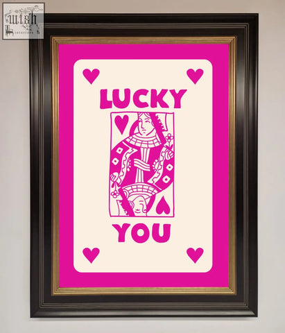 A hot pink framed poster featuring a vibrant queen of hearts playing card with lucky you text and gold matting