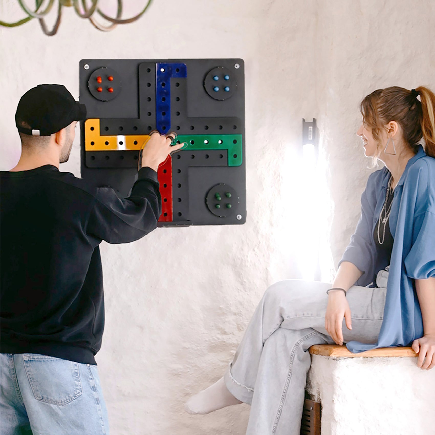 Black wall-mounted ludo wall game with colorful perforated red yellow green and blue playing paths and hanging instructions