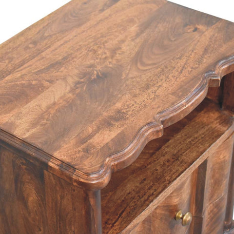 A rustic bedside table made of solid mango wood with a roasted almond finish and intricate carved edges