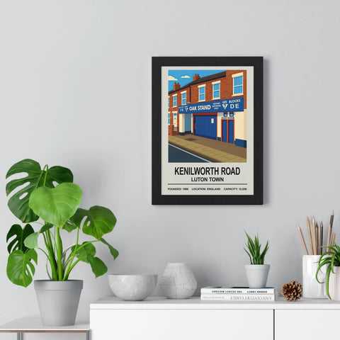 Black-framed vintage-style print of luton town kenilworth road stadium with blue storefronts and red brick buildings