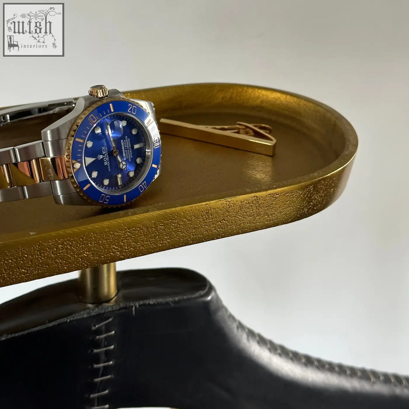 Rolex submariner watch with blue dial stainless steel case and gold accents shown on vintage brass coat hanger with leather shoulder pad