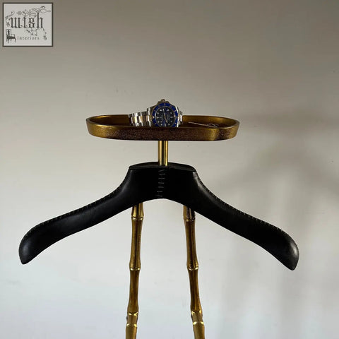 A silver blue rolex submariner with stainless steel bracelet on a black leather shoulder pad on vintage brass coat hanger