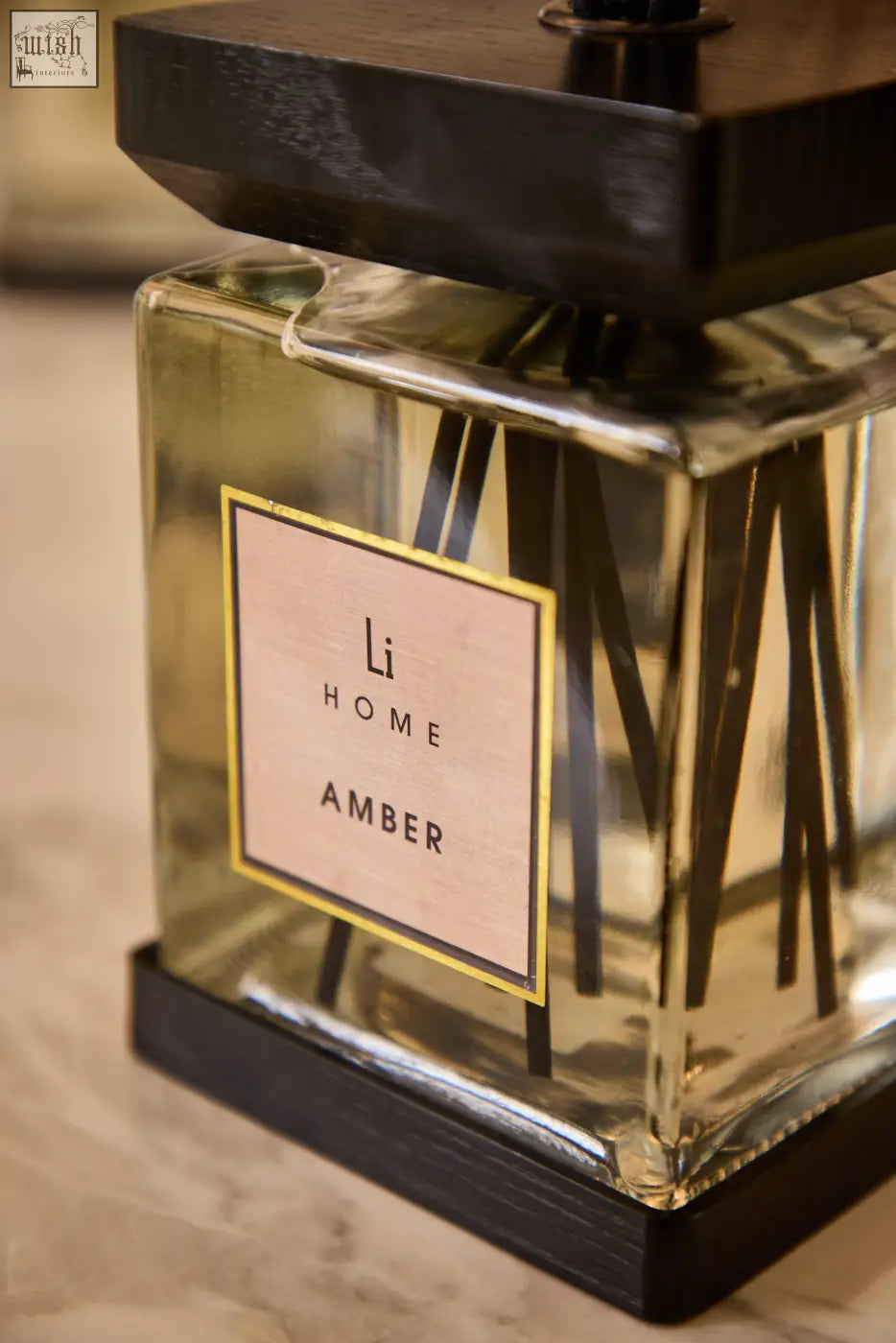 A luxury square glass diffuser with a black wooden top and base featuring amber-scented reeds