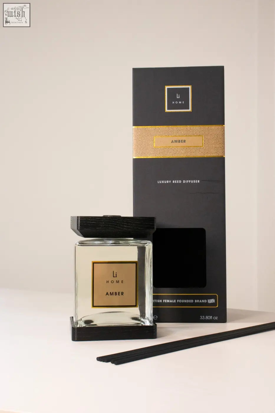 A sleek black and gold amber-scented reed diffuser from li home with a clear glass bottle and dark wood lid