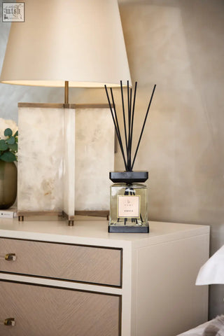 A sleek transparent glass luxury square diffuser with amber scent and black l’occitane label and base