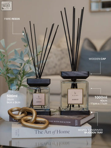 Two luxury square diffusers with black reeds and dark wooden caps labeled li homs amber on beige labels