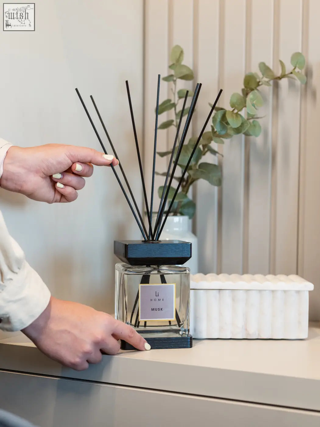 A sleek glass luxury square diffuser with dark blue wooden base black reeds labeled musk by l’occitane