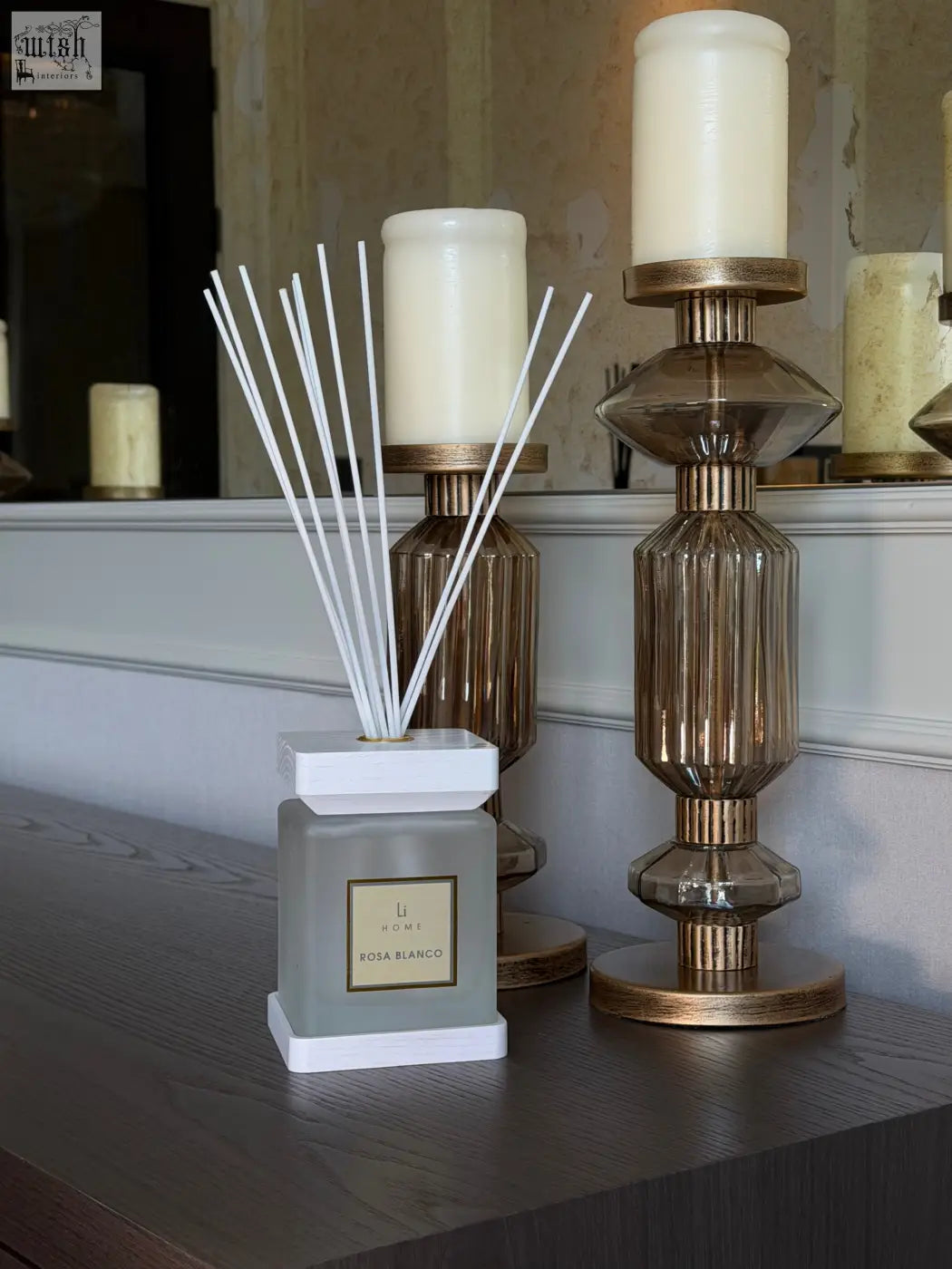 A sleek matte gray square reed diffuser with white base and rosa blanco gold label by li home for white rose scent