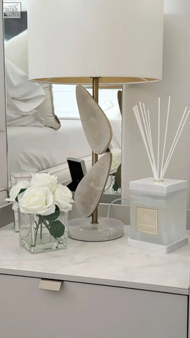 A sleek luxury square diffuser rosa blanco with a white rose scent and gold leaf-shaped metallic accents on base