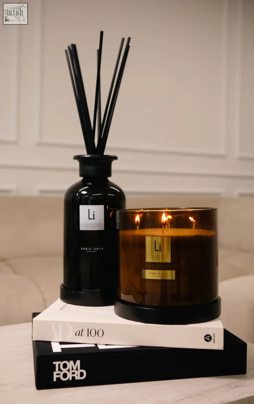 Black glass reed diffuser with slender reeds and silver label beside amber fie luxury xxl candle in amber glass