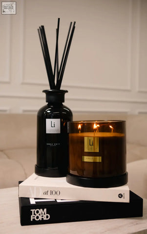 Black glass reed diffuser with slender reeds and silver label beside amber fie luxury xxl candle in amber glass