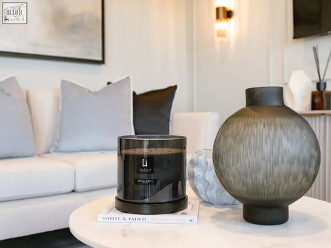 A sleek luxury xxl candle sable onyx in a black glass jar with dark wax sitting on a book on a marble table