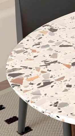 A lynette dining table with a round terrazzo top featuring white gray and warm brown speckles in a polished finish
