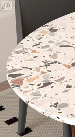 Round lynette dining table with a terrazzo top featuring white gray and warm brown speckles in a polished finish