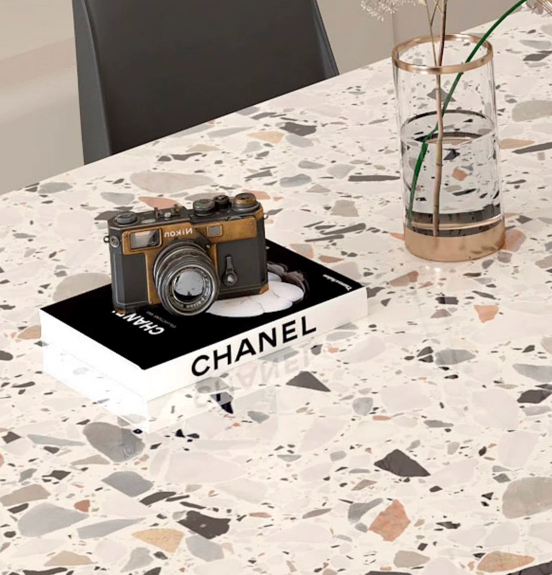Vintage-style black and gold nikon camera resting on a chanel book next to the lynette terrazzo oval dining table