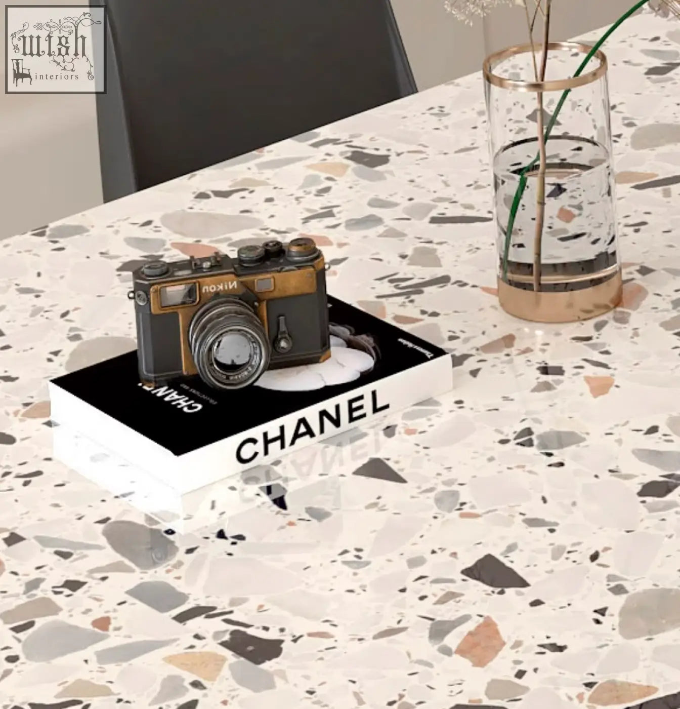 Vintage-style nikon camera with black and gold body resting on chanel book next to lynette terrazzo dining table