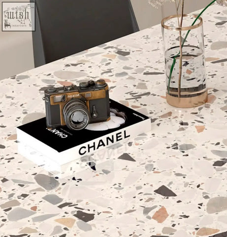 Vintage-style nikon camera with black and gold body resting on chanel book next to lynette terrazzo dining table