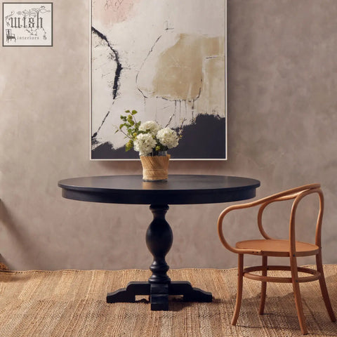 Black round dining table with turned pedestal base and ornate footrest paired with natural beech wood dining chair