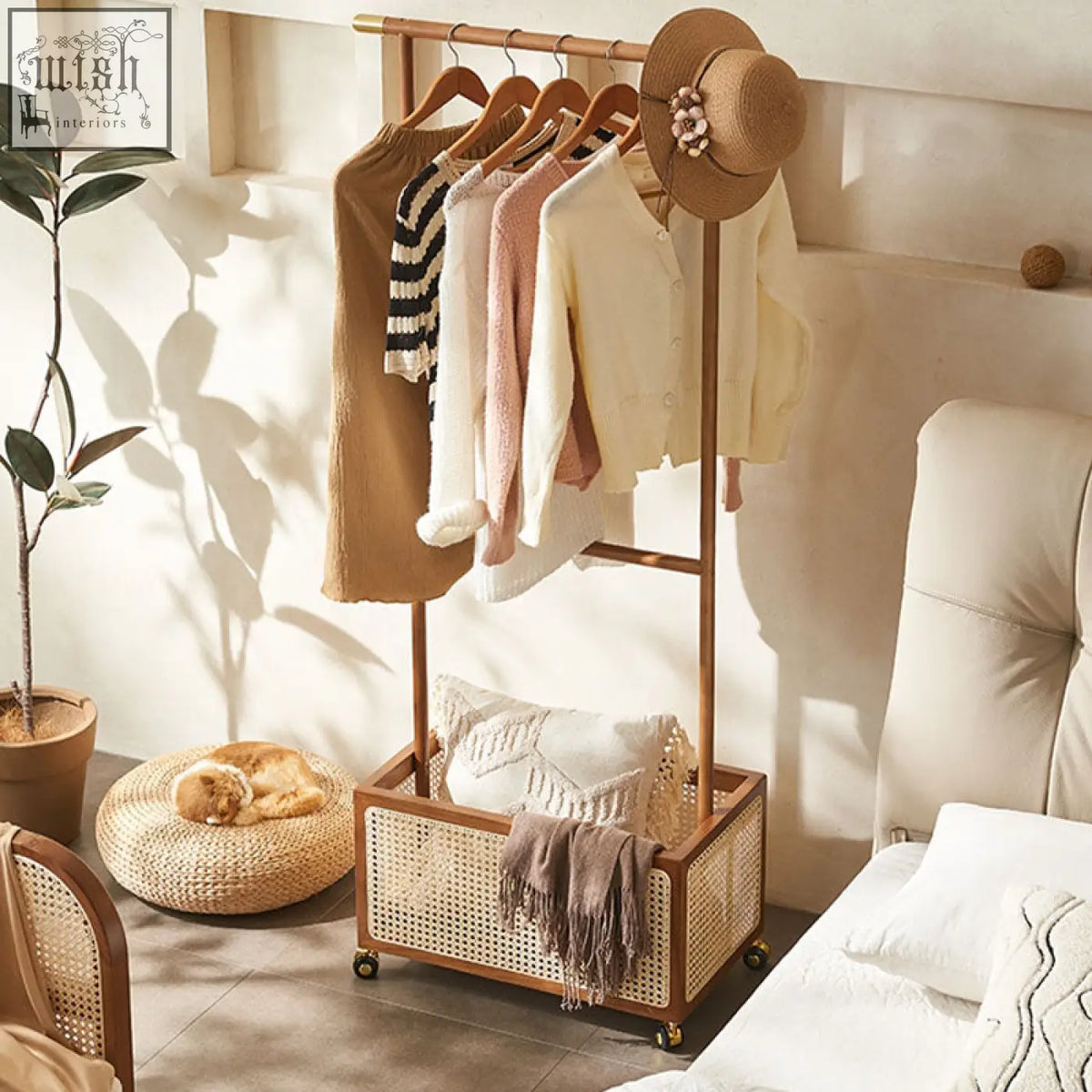 Wooden and rattan madeline coat rack with woven basket base holding pastel sweaters and a straw hat on top
