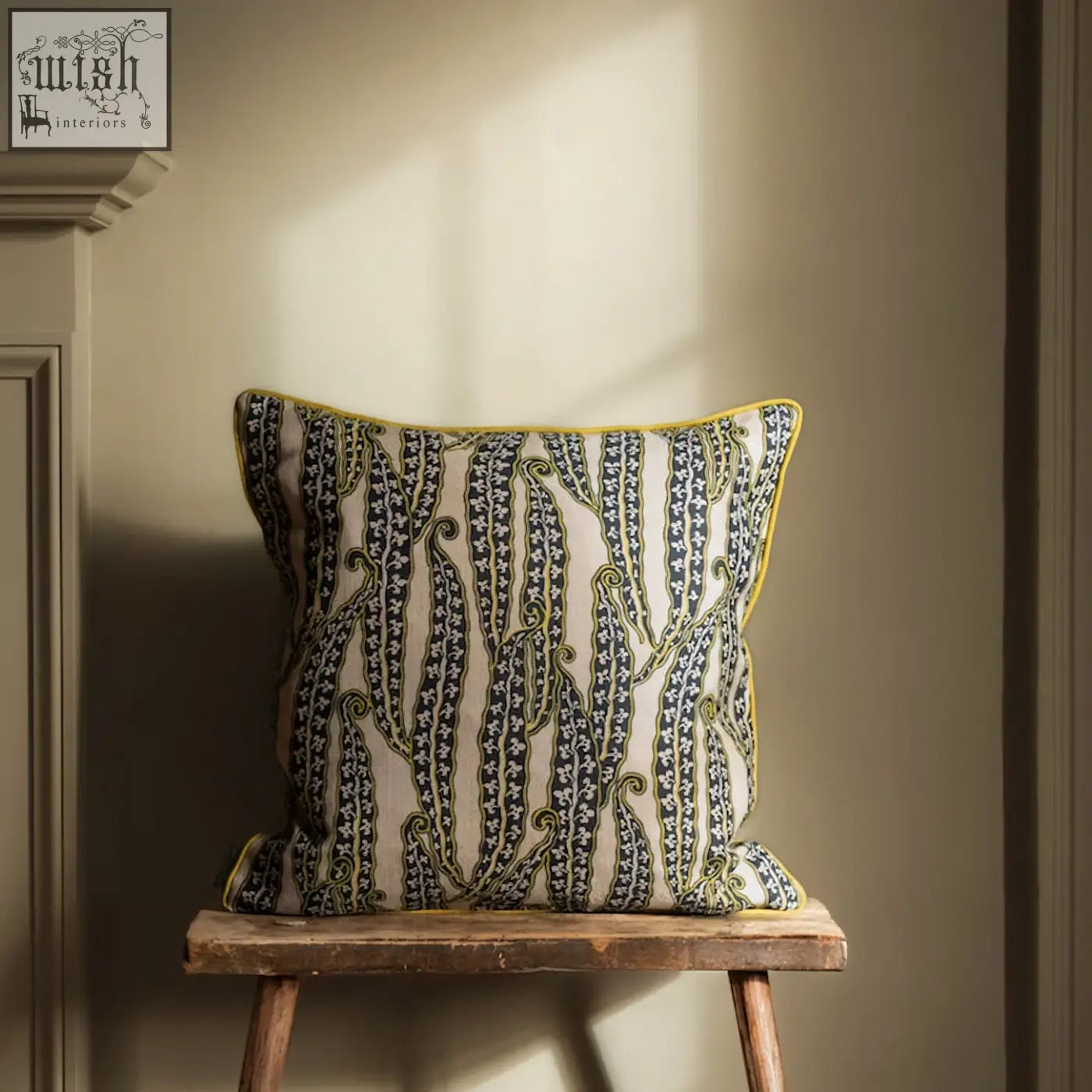 A magic beans cushion with cream base, navy blue and olive green paisley bands, and bright yellow trim