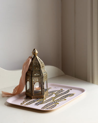 Antique brass moroccan lantern with intricate cut out patterns and peach ribbon on magic beans wooden tray