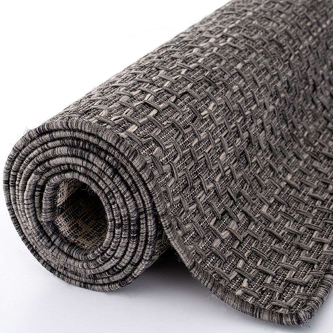 A rolled-up dark grey magic outdoor rug with a woven textured pattern perfect for outdoor use
