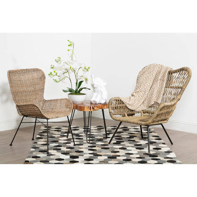 Woven wicker manado curved design natural rattan chair with black metal legs and a cozy throw on the seat