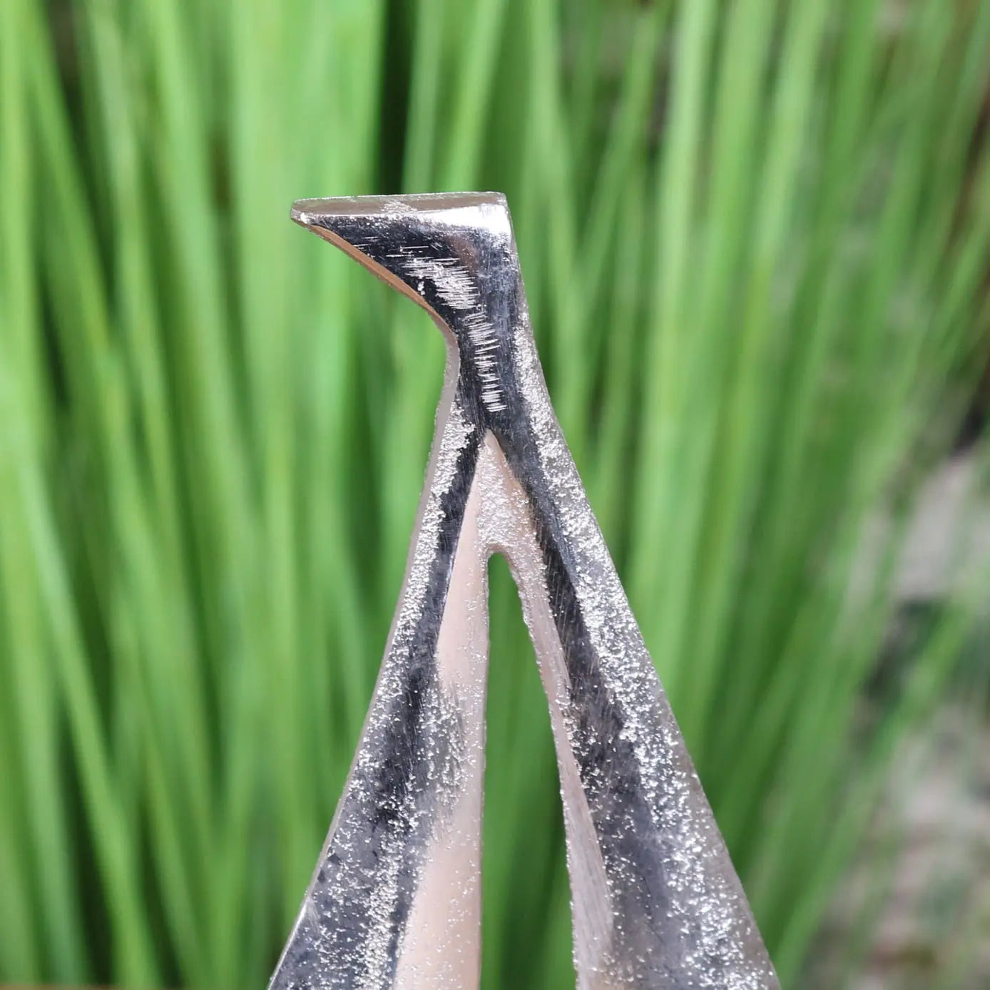 Silver metal nail clipper with sharp angled tip and textured surface shown with mandvi sailing boat ornament model