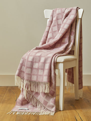 A soft pink and cream manhattan pure wool throw with intricate square checkered pattern draped on a white chair