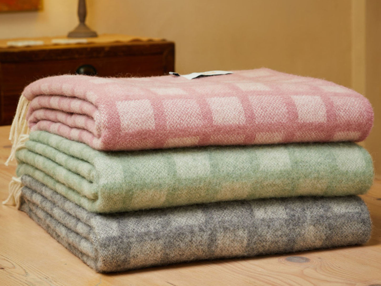 Stack of three manhattan pure new wool throws in soft pastel plaid with fringed edges featuring intricate square patterns