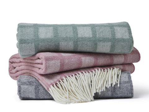 Stack of three folded manhattan pure new wool throws in muted pastel tones with intricate square plaid and fringe detailing
