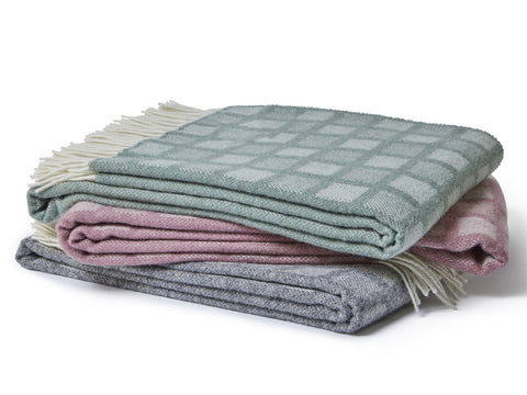 Stack of three folded manhattan pure new wool throws in muted pastel tones with intricate square patterns and fringed edges