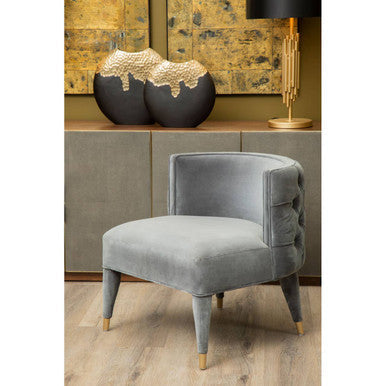 Gray velvet armchair with tufted back and gold-tone legs next to a manor table lamp with drum shade
