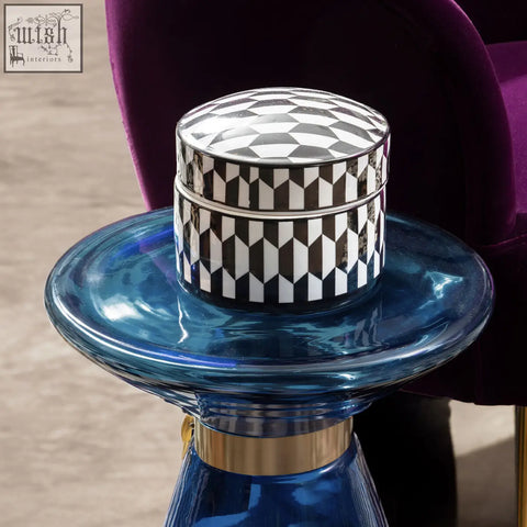 A marlo large black and white geometric print ceramic trinket box with a sleek cylindrical design on a blue glass table