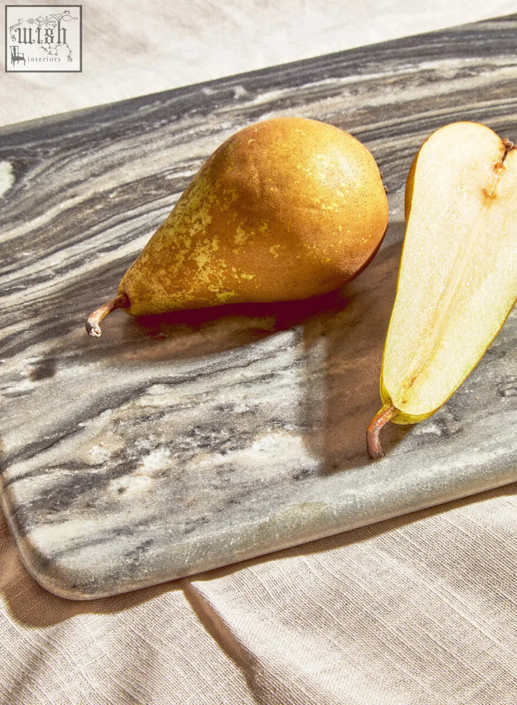 A golden-yellow pear with speckled skin beside its half on a marmore rectangular black marble chopping board
