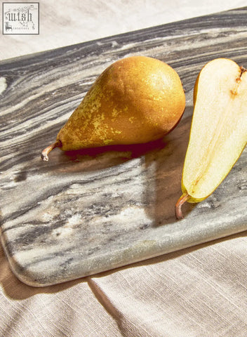 A golden-yellow pear with speckled skin beside its half on a marmore rectangular black marble chopping board
