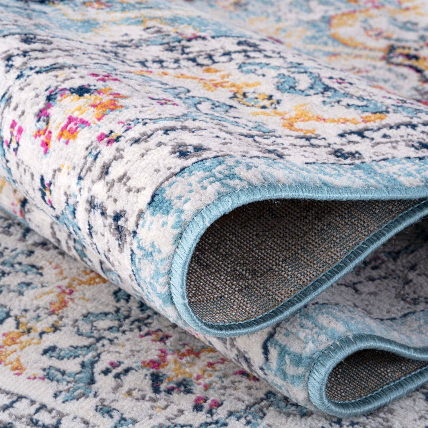 A rolled-up marrakech vintage rug with floral paisley patterns in soft blues creams pinks and yellows on white background