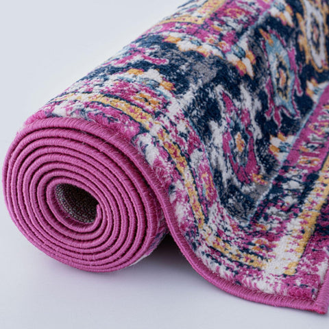 A marrakech vintage rug rolled up with a vibrant pink border and multicolored navy blue yellow magenta pattern