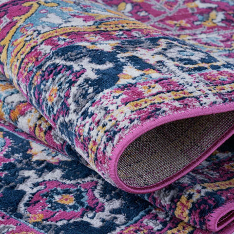 A rolled-up marrakech vintage rug with bold floral paisley pattern in pink navy yellow white and bright pink border