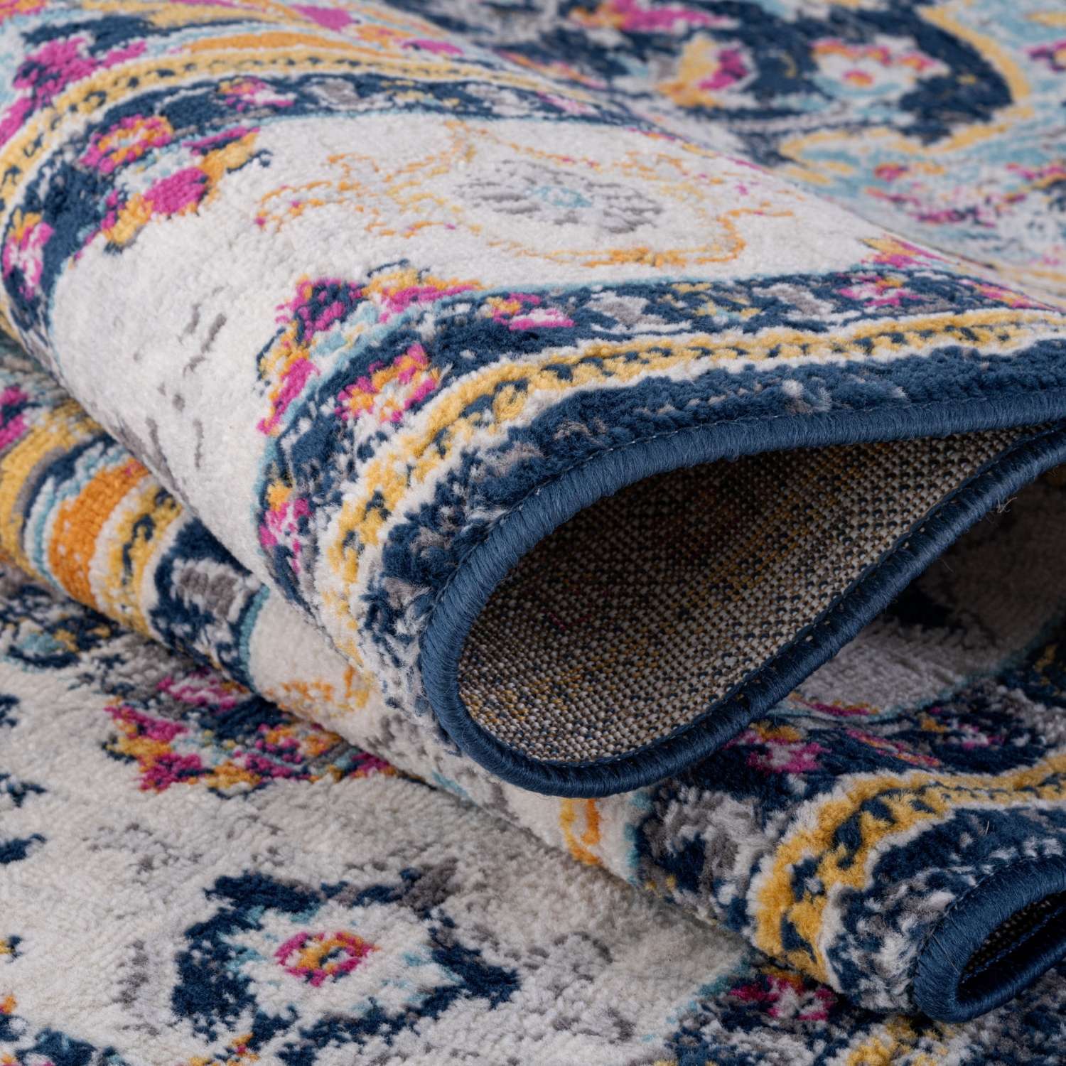 A plush rolled-up marrakech vintage rug with intricate floral paisley patterns in navy cream pink yellow and gray tones