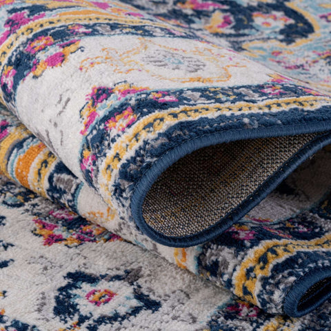 A plush rolled-up marrakech vintage rug with intricate floral paisley patterns in navy cream pink yellow and gray tones