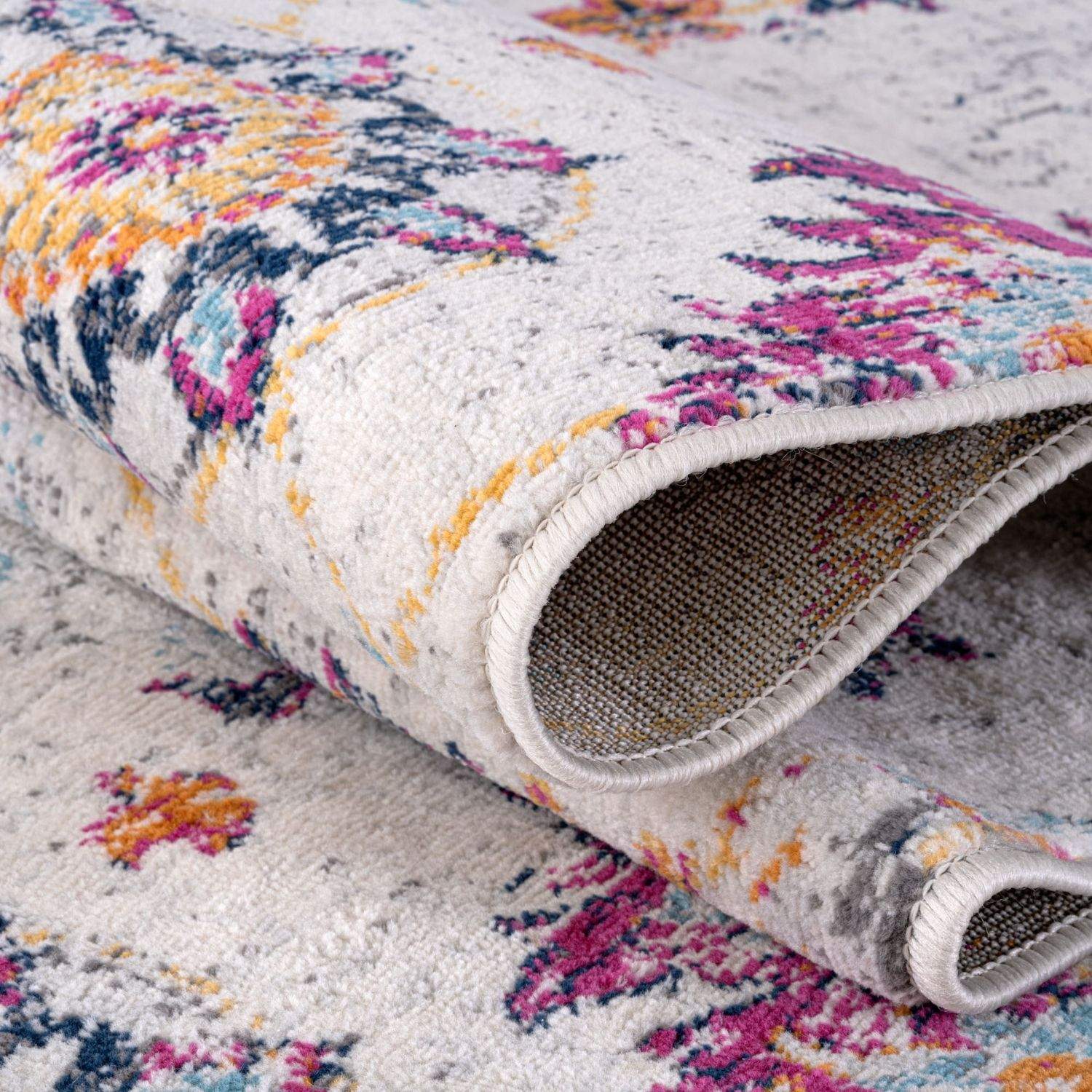 A plush rolled-up marrakech vintage rug with vibrant pink orange blue floral pattern on textured off-white base