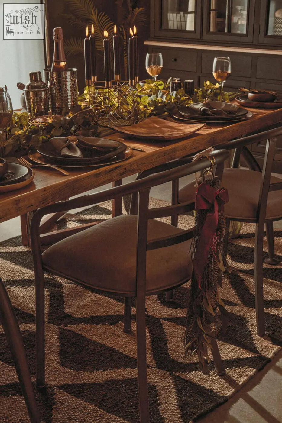 Rustic wooden dining table with dark metal legs featuring a martina hexagonal candle holder with greenery