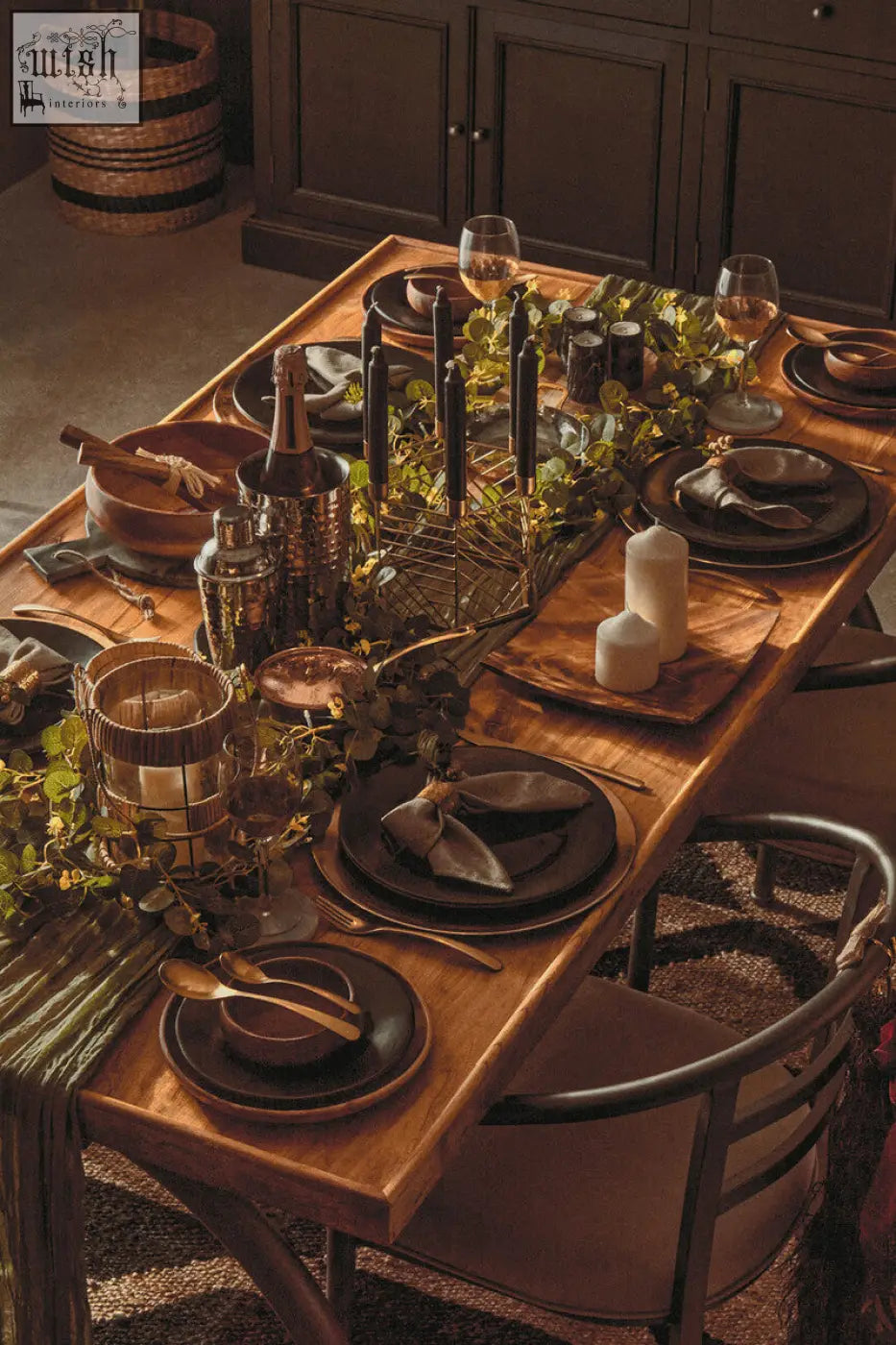 Rustic wooden dining table with dark plates metallic cutlery and green foliage centerpiece featuring martina hexagonal candle holder