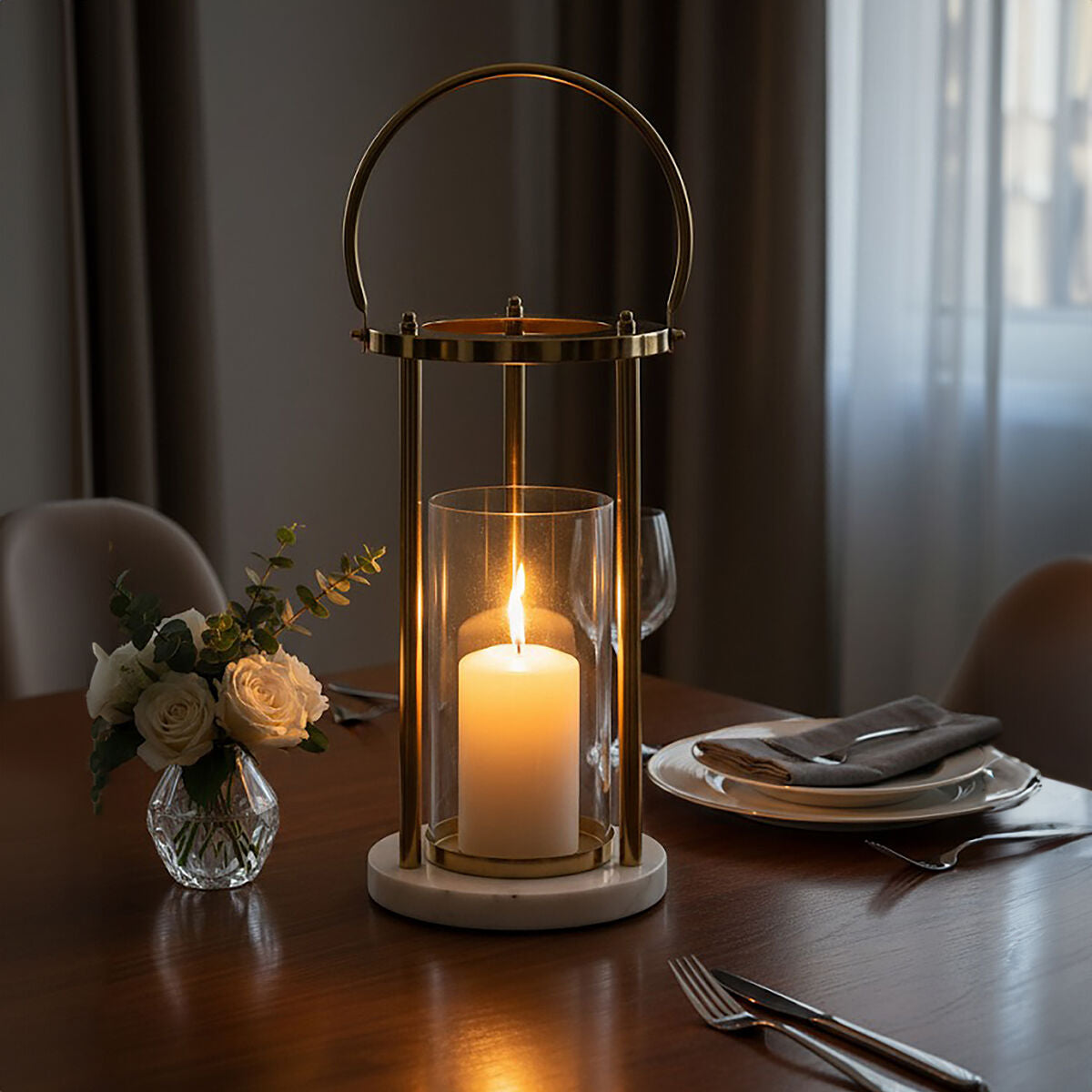 A brass martina medium hurricane lamp with handle featuring a clear glass cylinder white candle and white marble base