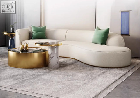 Cream-colored curved sectional sofa with green pillows paired with a mason marble coffee table set with marble coffee table