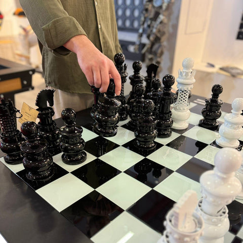 Glossy black and white ornate chess pieces on a reflective archtwain masterpiece chess table checkered board