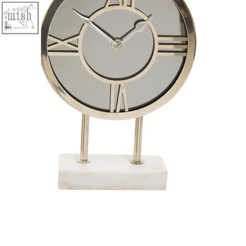 Silver-framed clock with roman numerals and mirrored face standing on a white marble base with marble base design