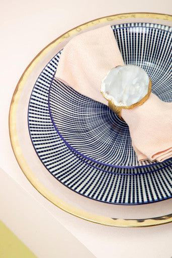 A navy blue and white striped plate with a gold rim and pink napkin from the maya 12 piece blue and white dinner set