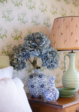 A green rattan mayfair tray hold all basket with a blue and white porcelain vase holding dried hydrangeas